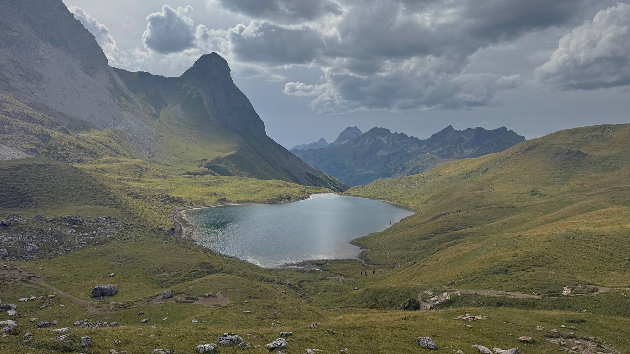 Ruhiger Bergsee in einem grünen Talkessel unter Wolken – Ruhe im Kalender statt Terminchaos