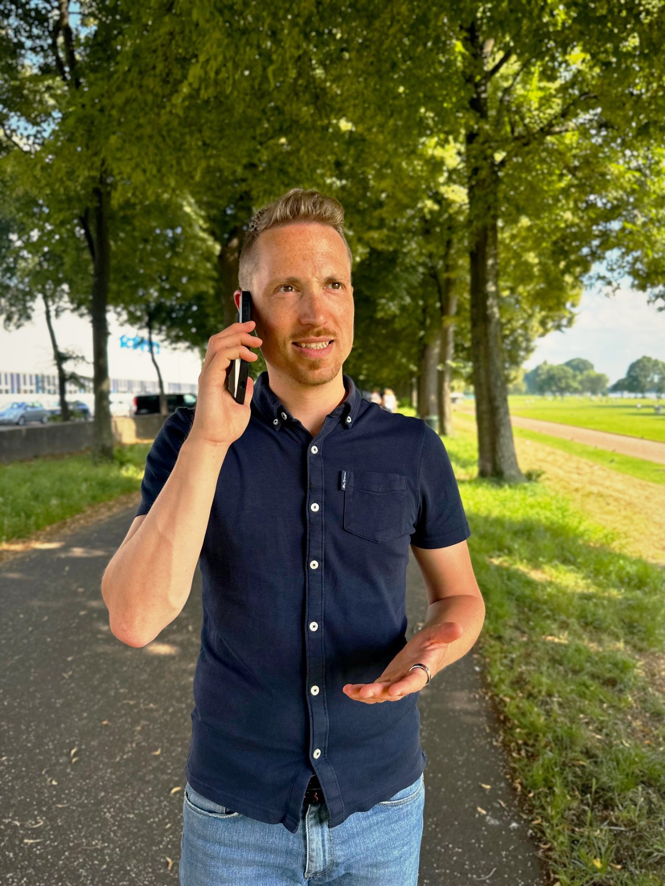 Christoph telefoniert auf einem sonnigen Weg unter Bäumen