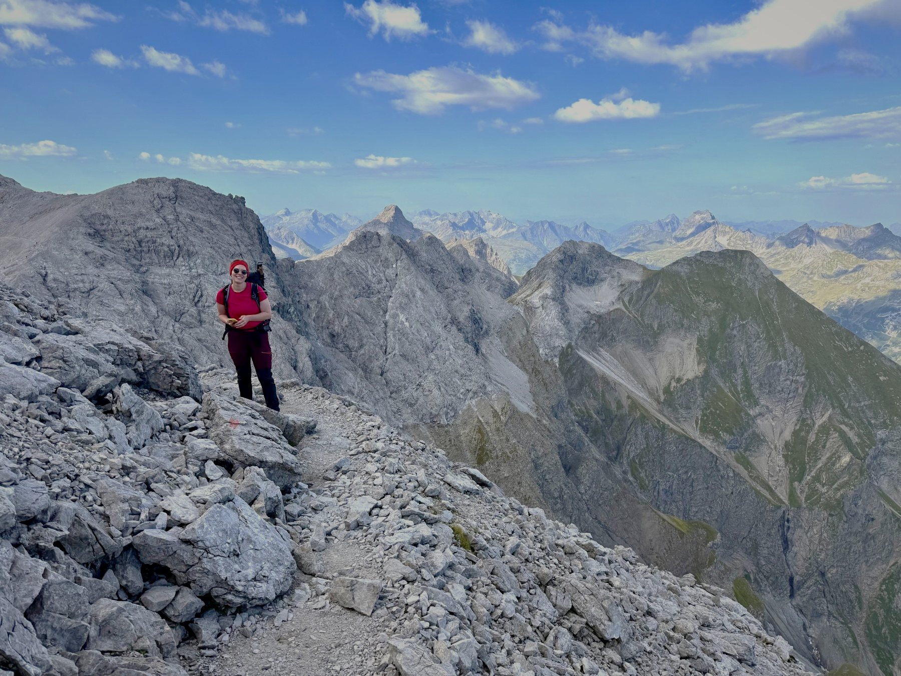 Katharina lächelnd auf einem Berggrat mit weitem Blick über die Alpen