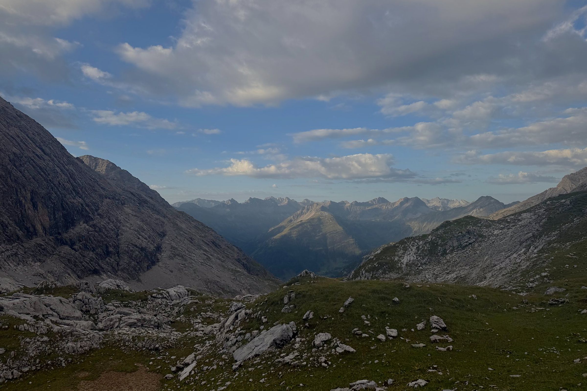 Weiter Blick über eine Almwiese mit Felsen auf Bergketten unter Wolken – in Ruhe klären, bevor Du KI einführst