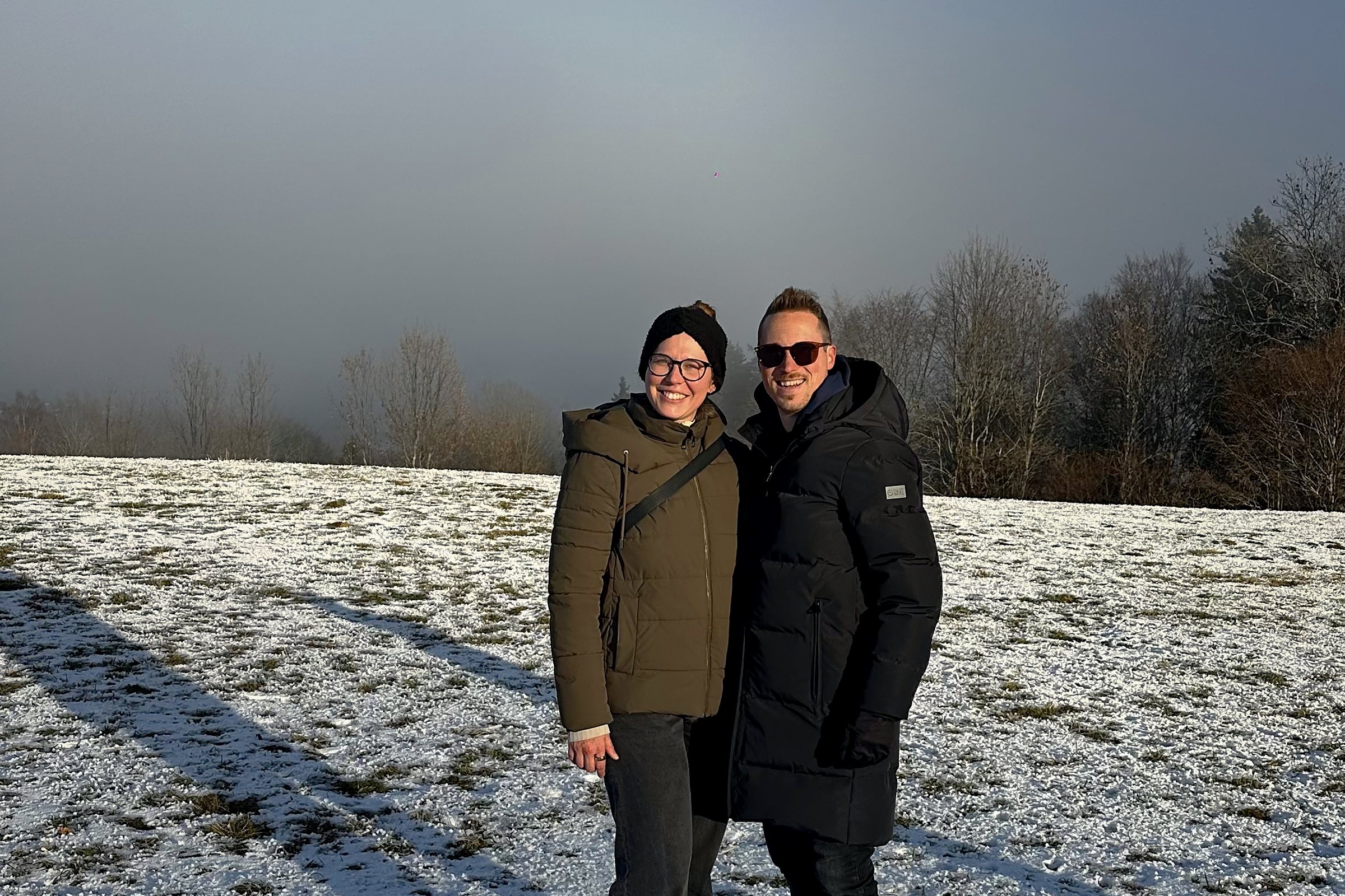 Katharina und Christoph stehen lachend nebeneinander auf einer verschneiten Wiese – echter Austausch gegen die Einsamkeit der Selbstständigkeit